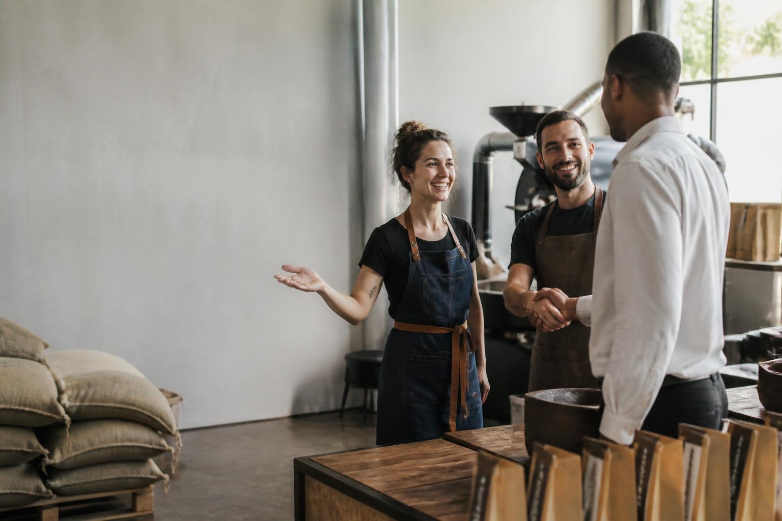Torréfactrice souriante présentant un confrère à un autre professionnel dans son atelier.